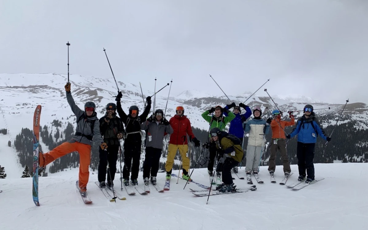 A group of FIRST RF employees on a "ski day" at the top of Arapahoe Basin in Colorado with their poles in the air.