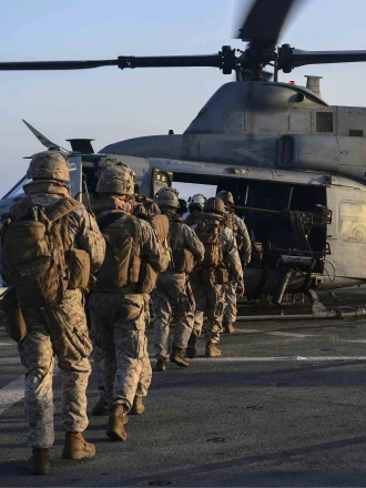 U.S. marines loading onto an AH-1Z Viper attack helicopter that sits on the flight deck aboard the amphibious dock landing ship USS Pearl Harbor (LSD 52).
