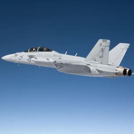 A U.S. Navy F/A-18 Super Hornet fighter jet in flight against a clear blue sky, viewed from the side.
