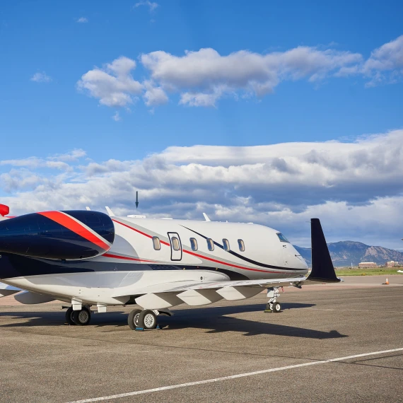 A plane on a runway on a sunny day with foothills in the background. Two white conformal looking antennas can be seen on the back belly of the airplane.