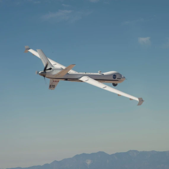 NASA's MQ-9 Predator banking to the right with mountains in the background and a perfectly blue sky taking up most of the background.