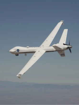 NASA's MQ-9 Predator banking in a blue sky with mountains in the background.